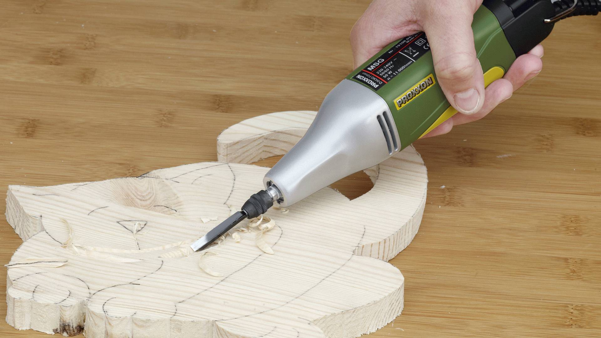 Eine Person verwendet ein Werkzeug, um eine Katzenform aus einem Holzbrett auf einer Holzoberfläche zu schnitzen.