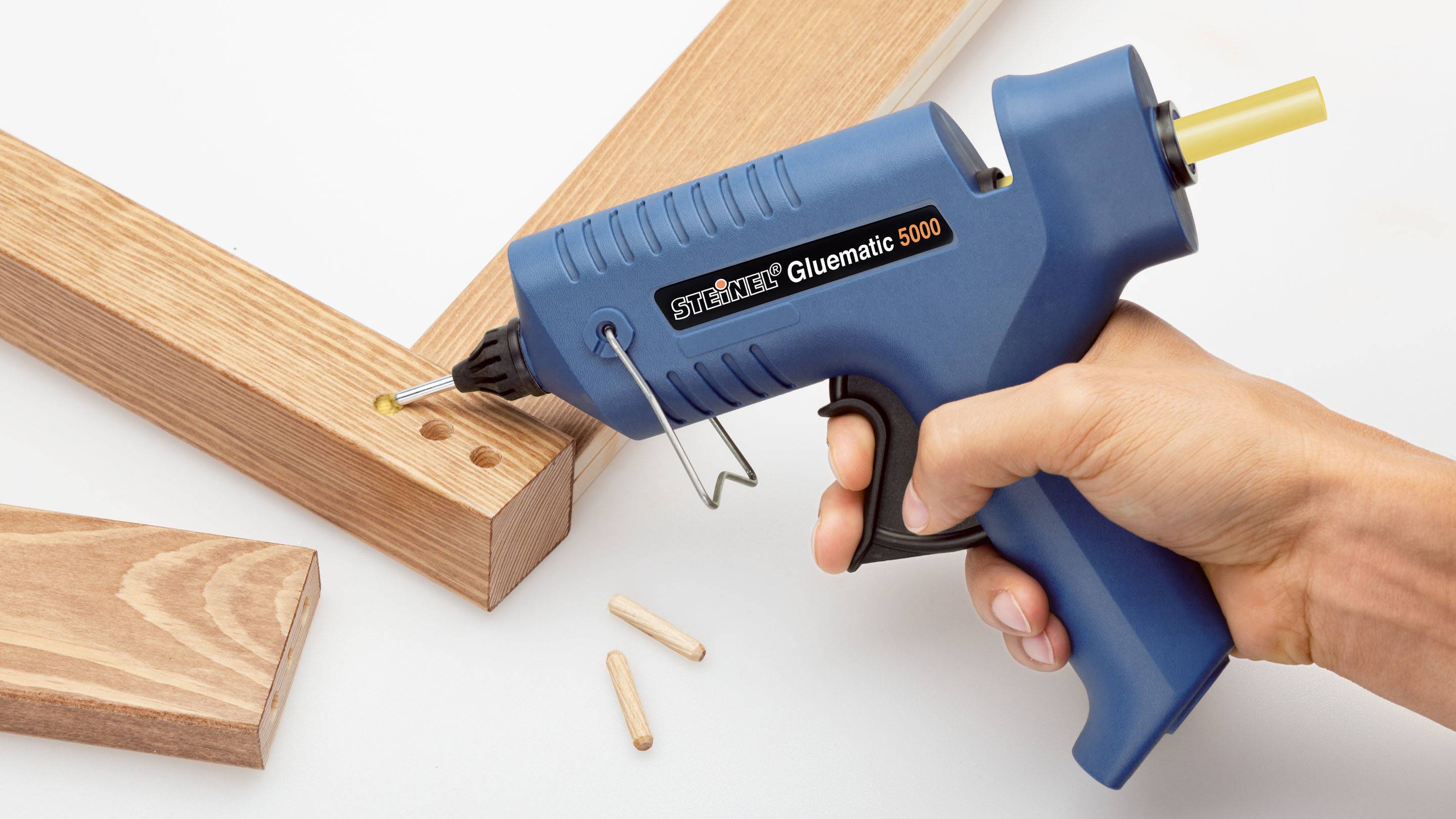 Eine Hand hält eine blaue Heißklebepistole, die bereit ist, Holzstücke mit Dübellöchern zu verbinden.