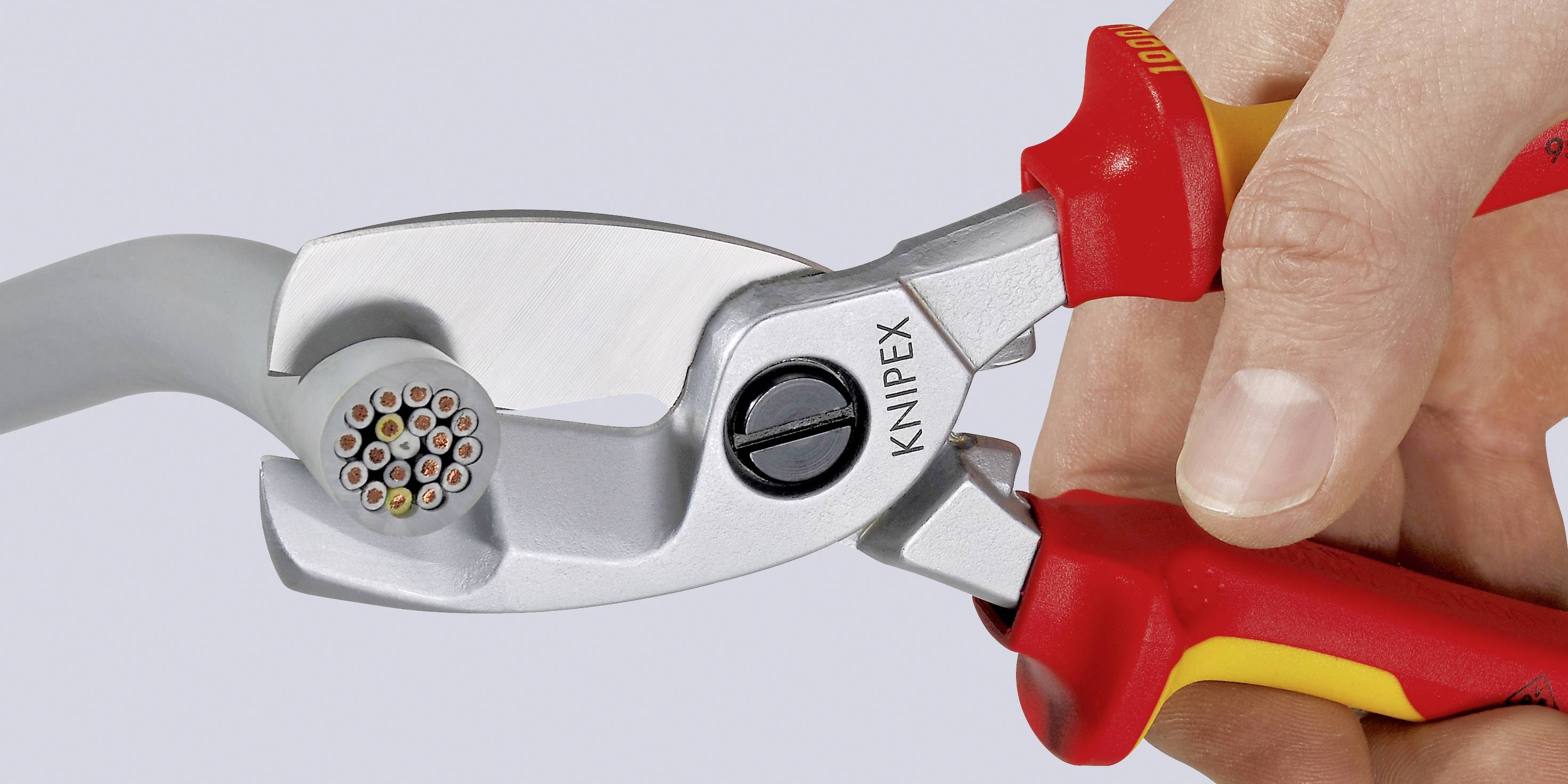 Eine Hand hält einen KNIPEX-Kabelschneider, der ein dickes Kabel durchtrennt. Der Schneider hat rote und gelbe Griffe.