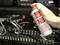 Eine Hand sprüht ein Druckluftspray auf einen Server-Schrank mit Kabeln und Blinklichtern, um Staub zu entfernen.