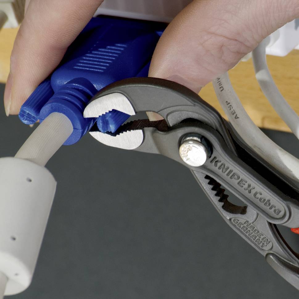 Eine Hand benutzt eine Zange, um einen blauen Stecker in ein weißes Kabel einzuführen.