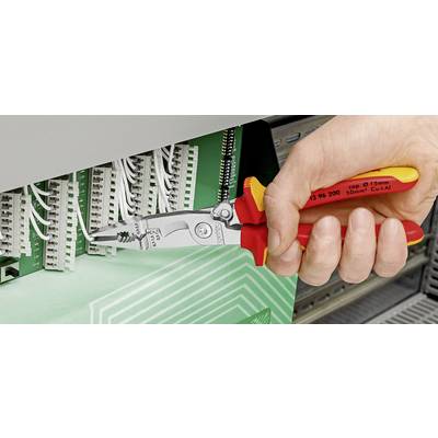 Eine Hand hält eine Zange, die an einem Kabel in einem Schaltkasten arbeitet. Mehrere weiße Kabel sind an einem grünen Panel angeschlossen.