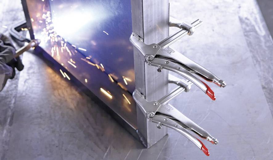 Eine Person schweißt Metallplatten, die mit Klemmen an einem Rahmen befestigt sind. Funken fliegen auf der linken Seite des Bildes.