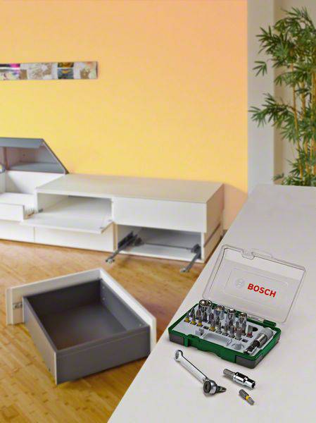 Ein offener Werkzeugkasten mit verschiedenen Bits und einem Schraubendreher liegt auf einem Tisch. Im Hintergrund sind Möbel im Aufbau.