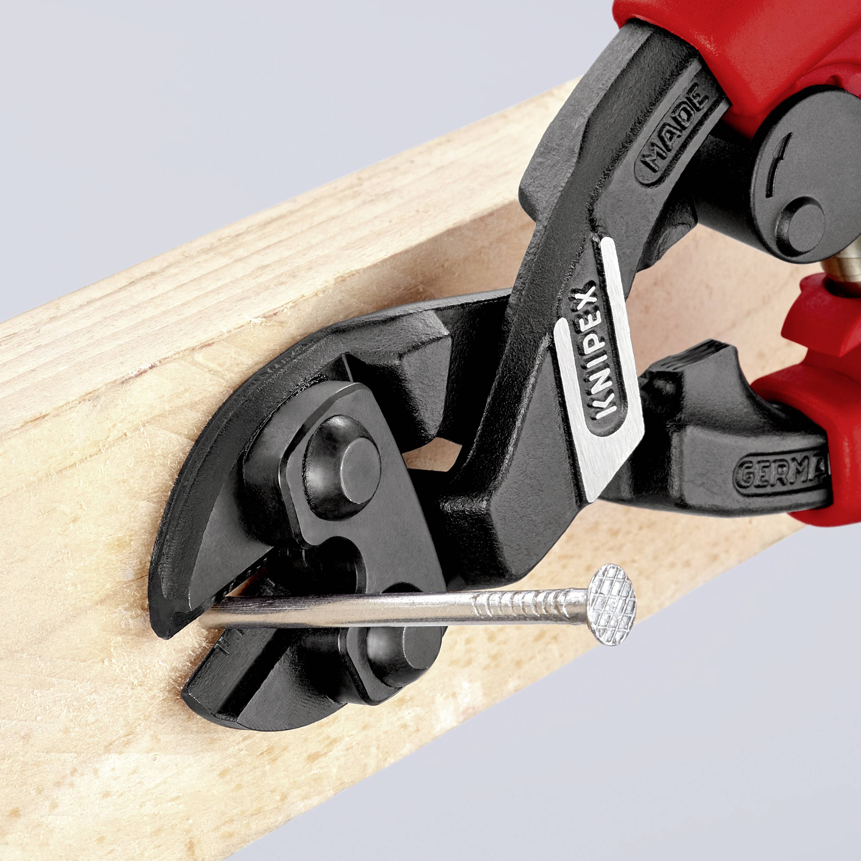 Eine schwarze und rote Zange von Knipex zieht einen Nagel aus einem Holzbrett.