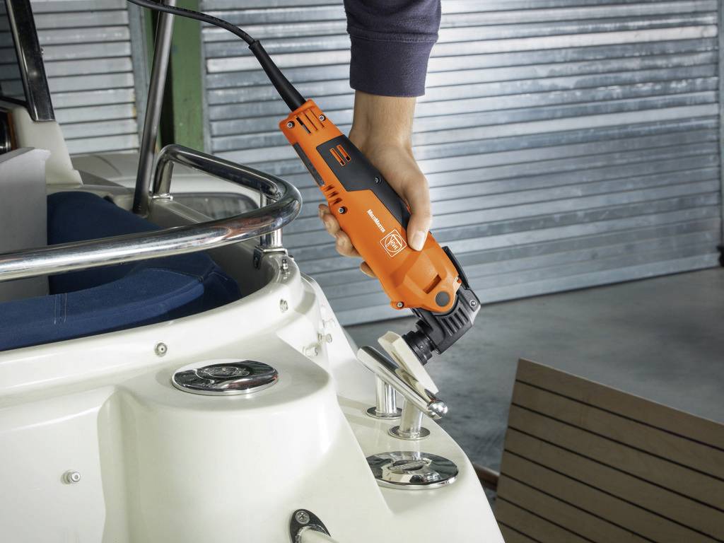 Eine Person schleift ein Metallteil auf einem Boot mit einem orangefarbenen Schleifgerät.