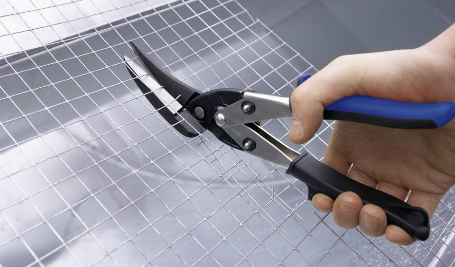 Eine Hand schneidet mit einer Blechschere ein Drahtgitter.