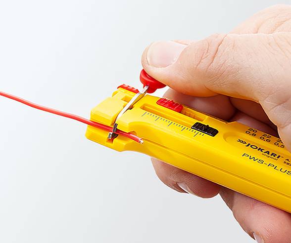 Eine Hand, die ein gelbes Abisolierwerkzeug verwendet, um die Isolierung von einem roten Kabel zu entfernen. Das Werkzeug ist mit 'PWS-PLUS' beschriftet.