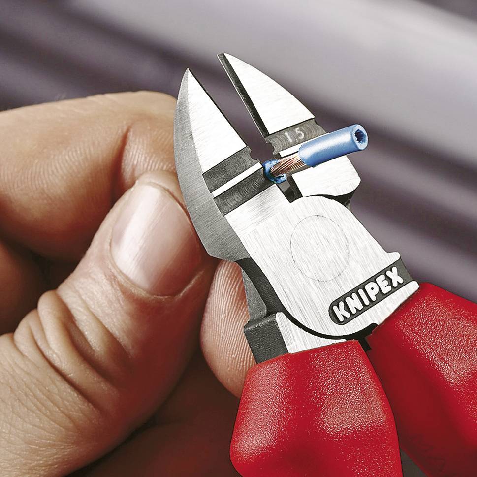 Hand hält eine rote, blaue und silberne Knipex-Zange, die ein Kabel schneidet. Fokus auf präzisen Schnitt und Details der Zange.