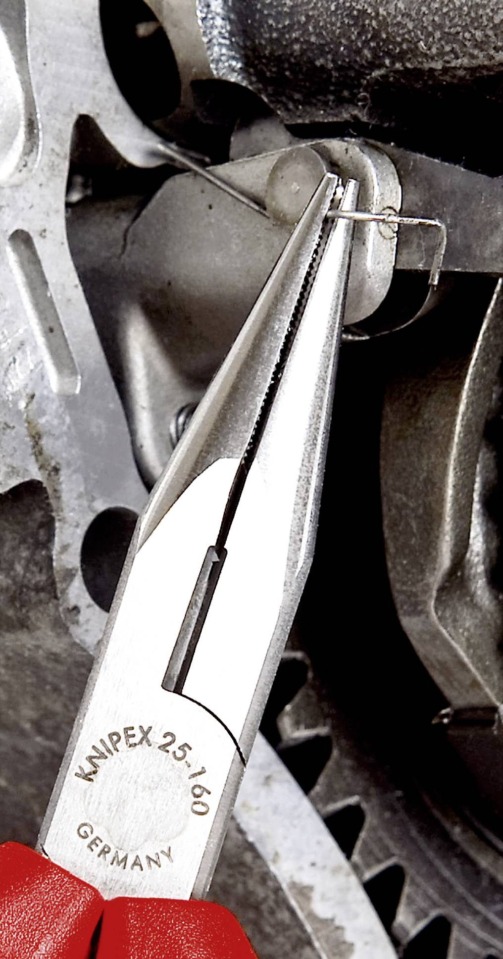 Nahaufnahme einer Zange, die eine kleine Metallklammer hält, vor einem mechanischen Hintergrund.