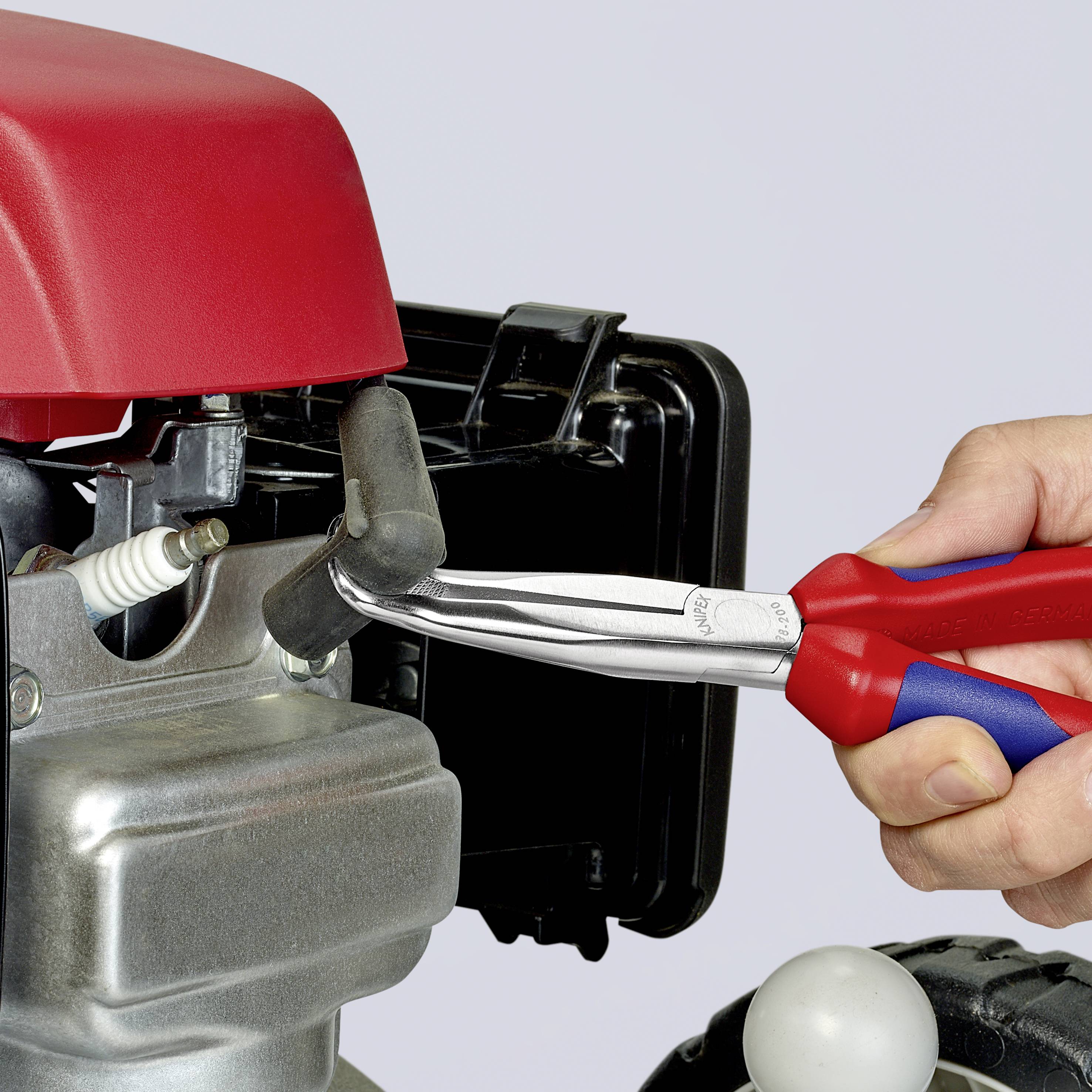 Hand hält Zündkerzenschlüssel und entfernt vorsichtig die Zündkerze aus einem kleinen Motor mit einer roten Abdeckung.