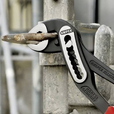 Eine Zange kneift ein Stück Metall, das durch einen Metallzaun ragt.