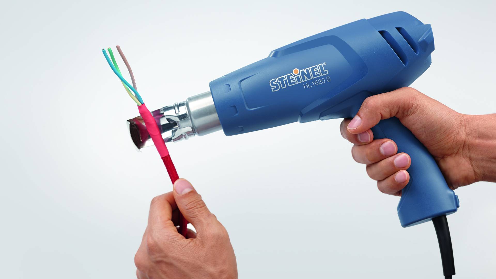 'Hand hält Heißluftgebläse, das auf Kabelhülle gerichtet ist, um sie zu erhitzen oder zu entfernen. Produkt für Elektrowerkzeugeinsatz.'