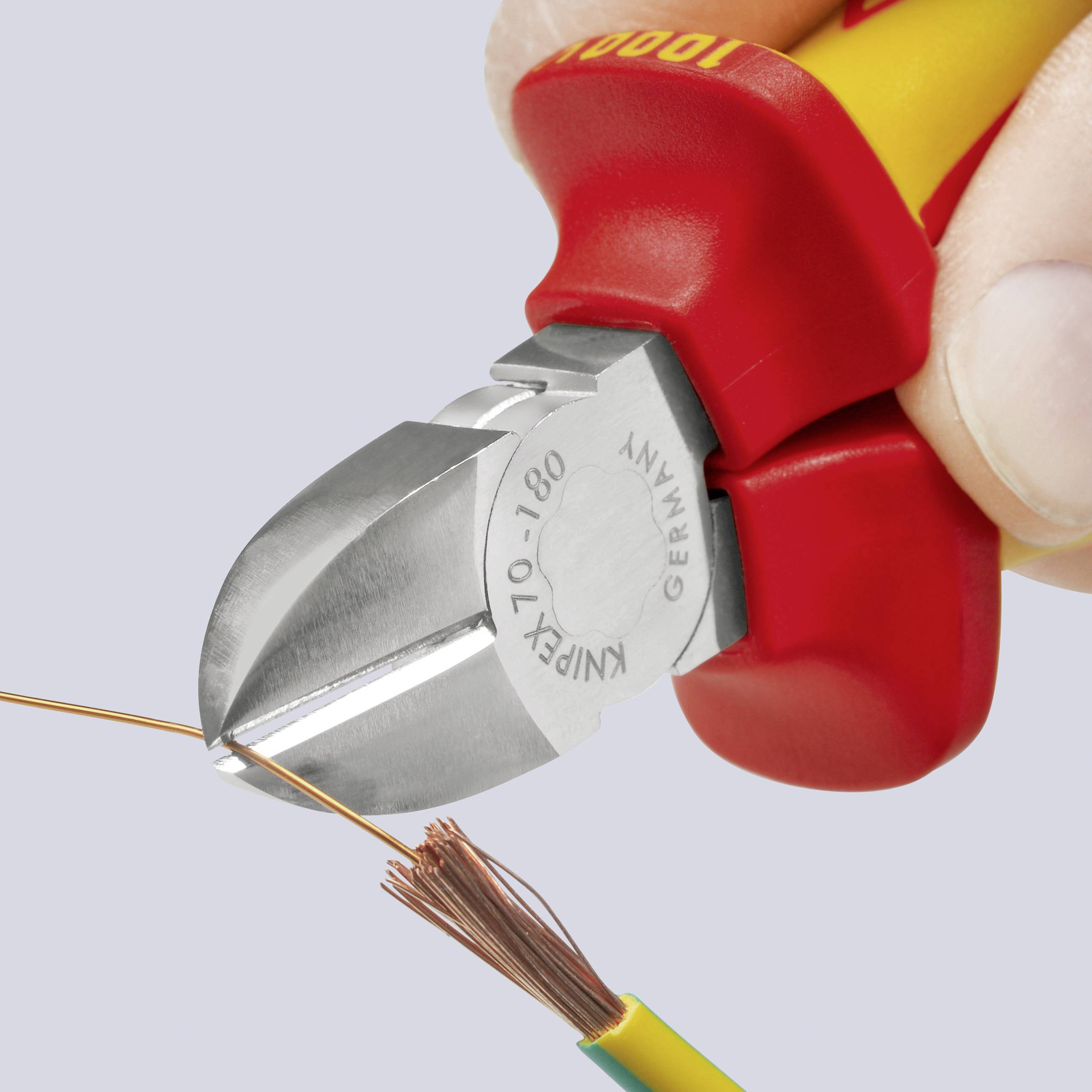 Hand hält einen roten Seitenschneider, der ein gelbes Elektrokabel mit grünem Streifen schneidet, wobei das Kupferinnere sichtbar ist.