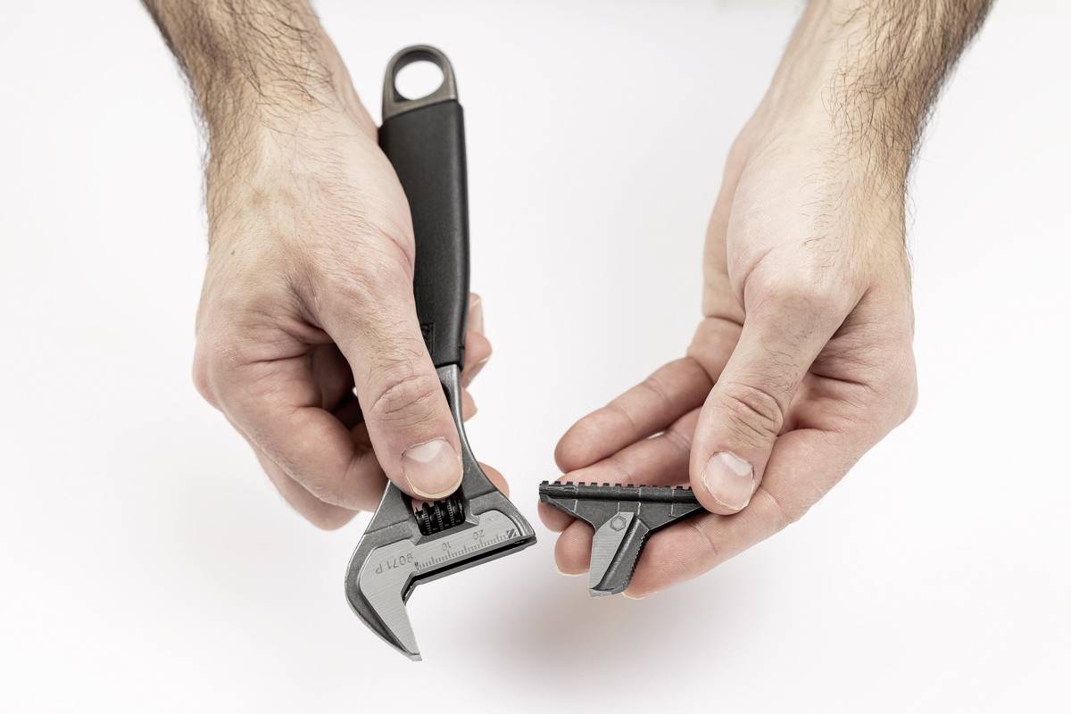 Zwei Hände halten einen verstellbaren Schraubenschlüssel und einen abgebrochenen Teil eines Kunststoffzahns, das bearbeitet wird.