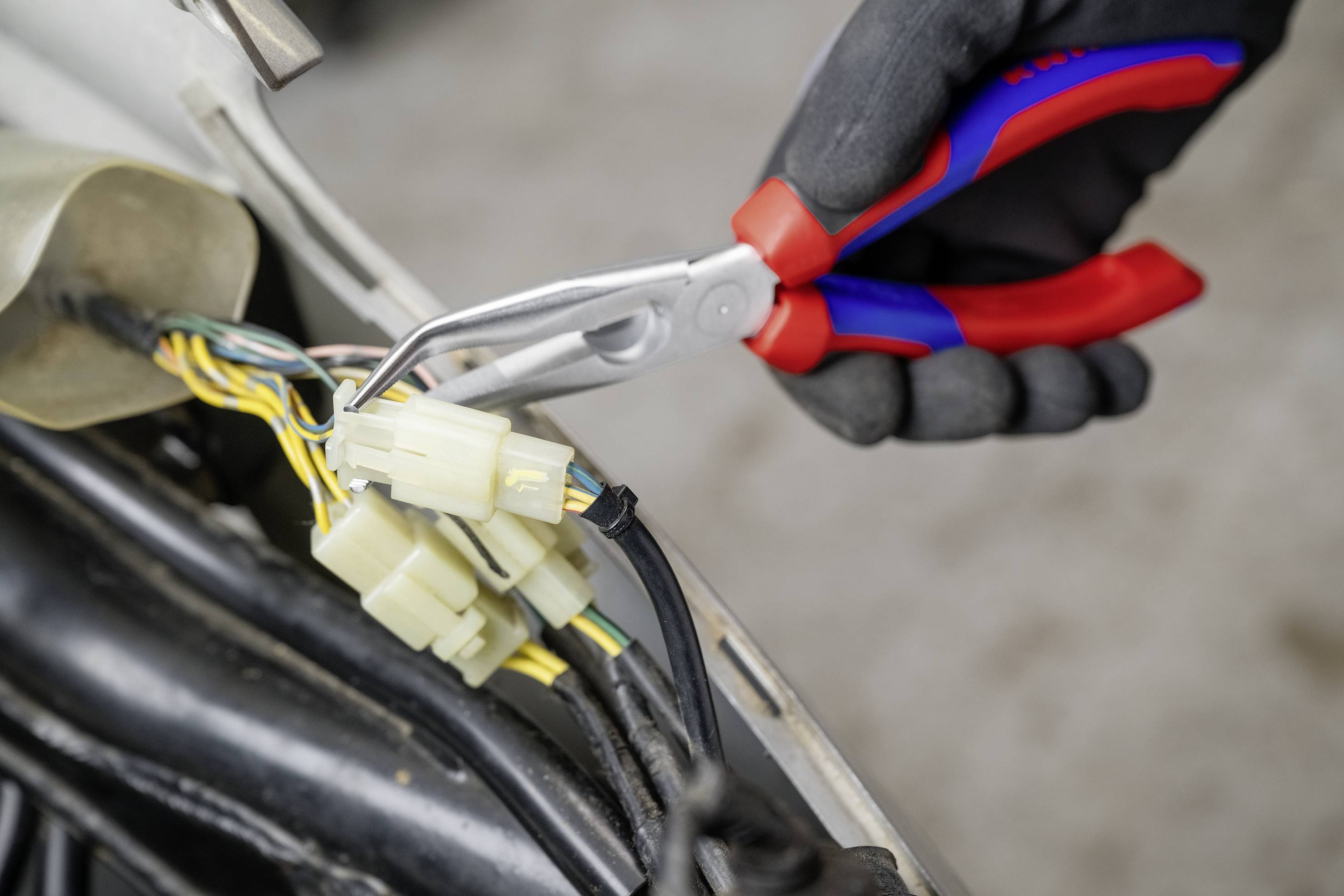Eine Hand hält mit einer Zange Kabel an einem elektrischen Anschluss. Mehrere bunte Drähte sind sichtbar.