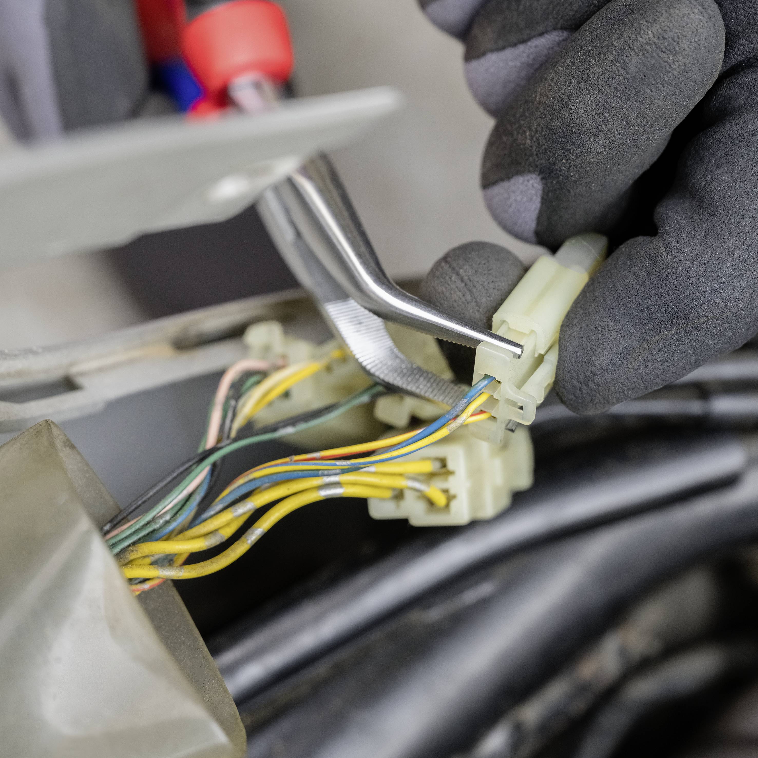 Zwei Hände mit schwarzen Handschuhen arbeiten an einem Kabelanschluss mit bunten Drähten, indem sie ein gelbes Kabel entfernen.