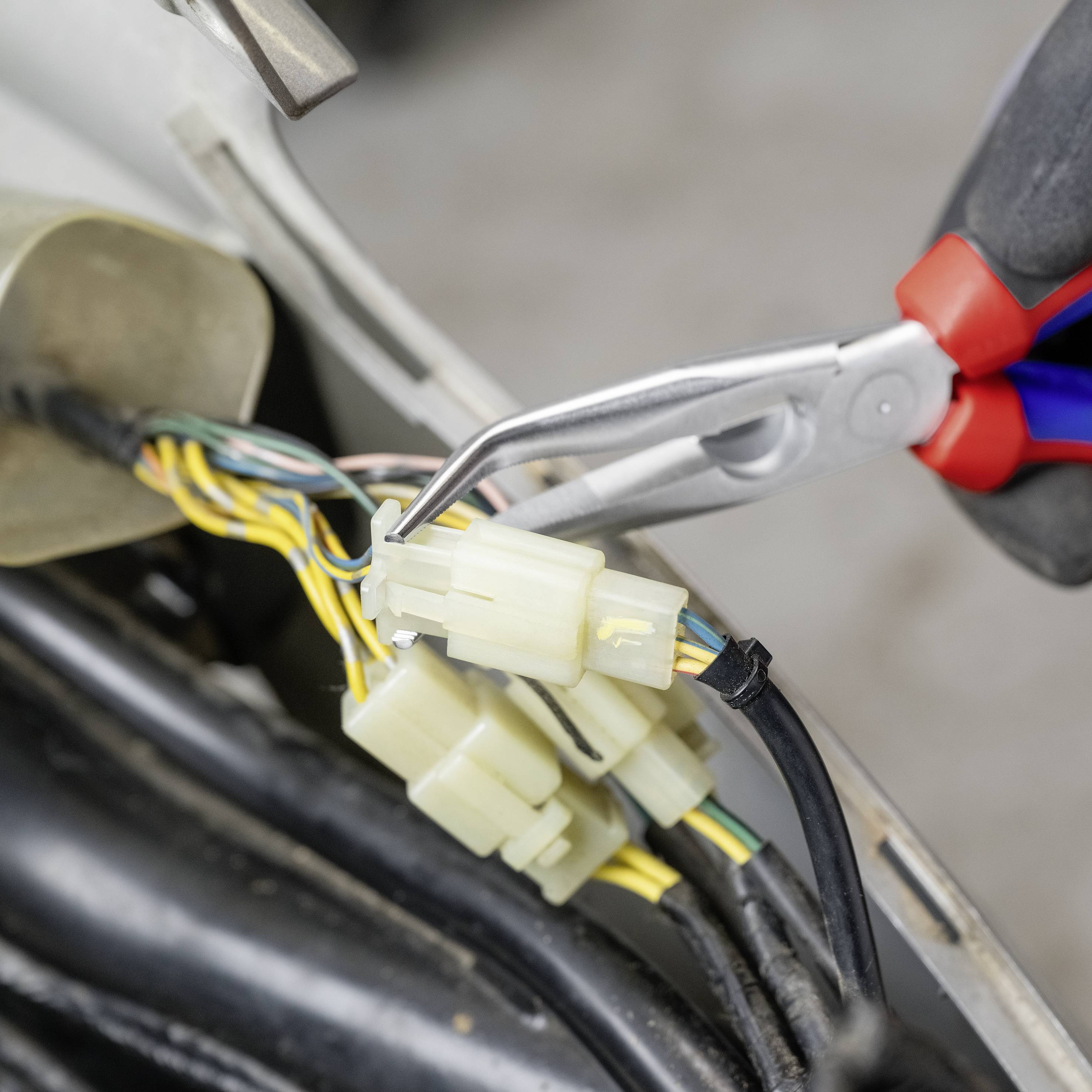 Nahaufnahme einer Hand, die mit einer Zange farbige elektrische Kabel in einem Fahrzeug bearbeitet.