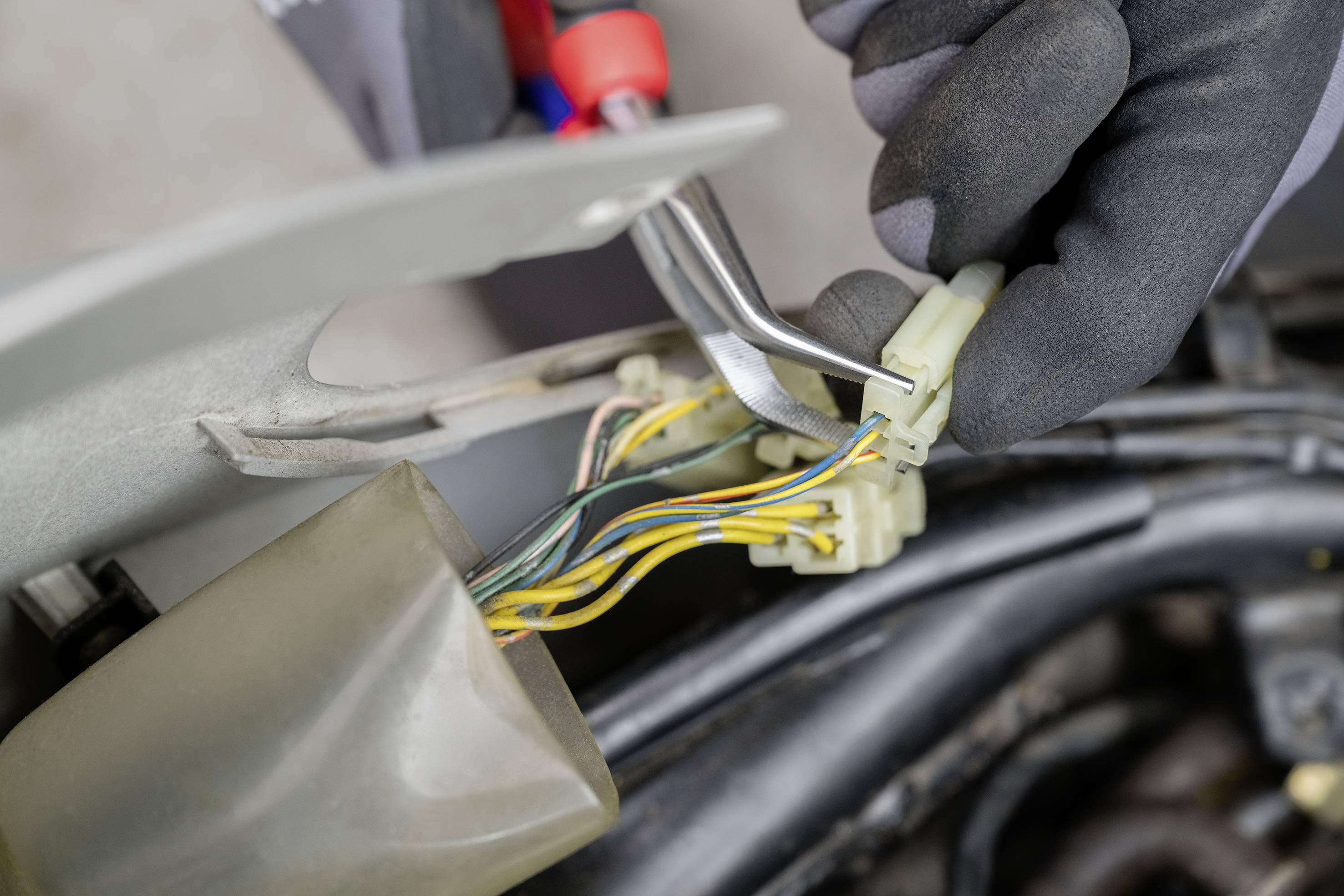 Eine Hand mit einem Werkzeug repariert oder installiert elektrische Kabel in einem Fahrzeug, fokusiert auf Drähte und Stecker.