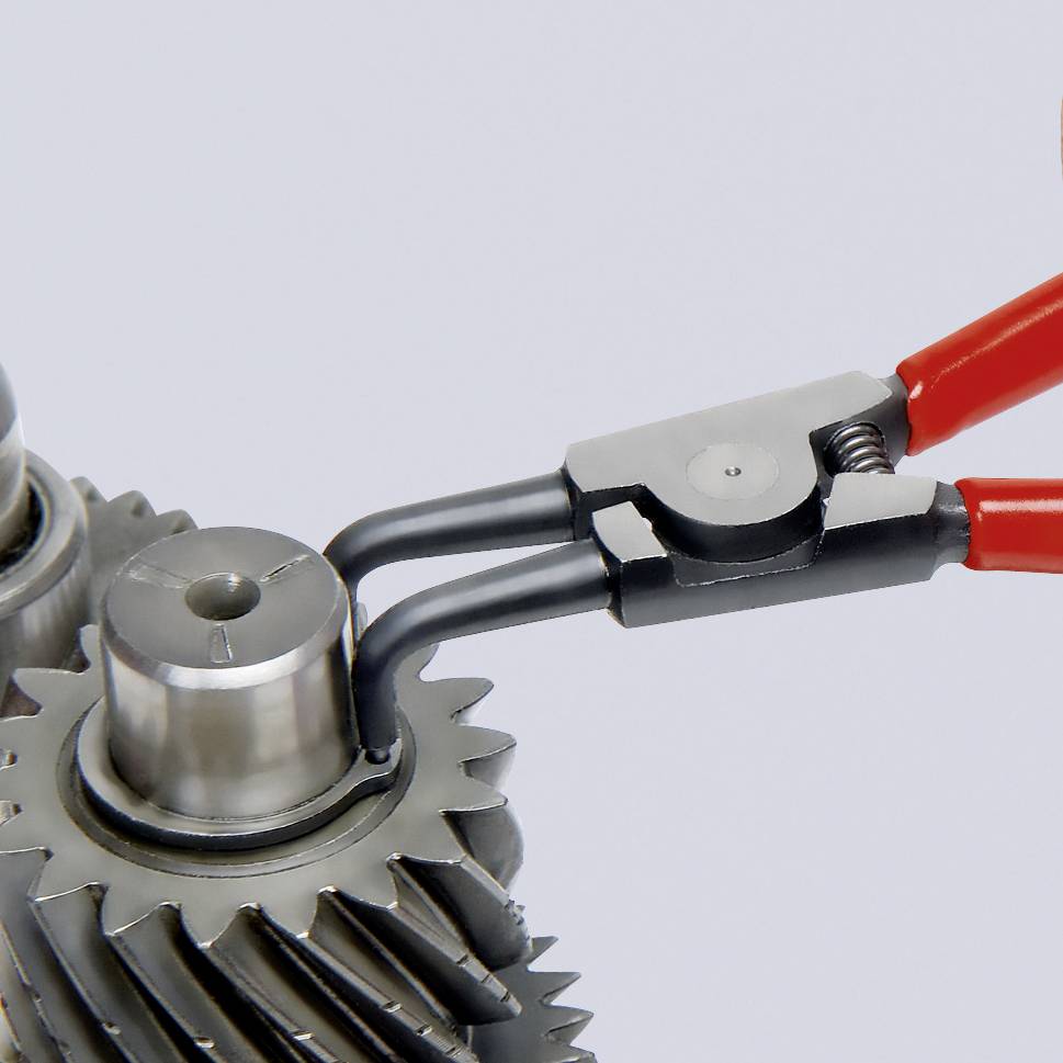 Zwei metallische Zahnräder, gedreht von einer Zange mit roten Griffen. Mechanische Präzision und technische Anwendung im Fokus.