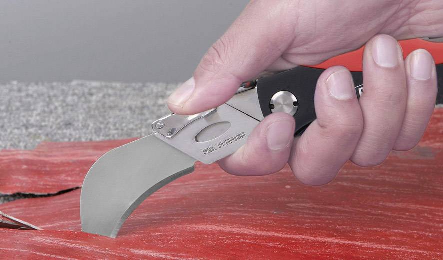 Hand hält ein Klappmesser mit gebogener Klinge, das roten Stoff schneidet. <br><br>