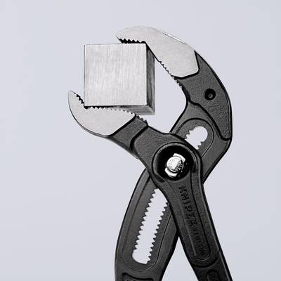 Eine Zange hält eine metallische Würfelform. Die Zange hat geschwungene Griffe und zeigt das greifende Maul in Nahaufnahme.