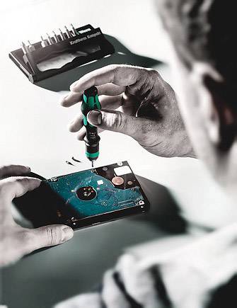 Eine Person repariert eine Festplatte mit einem Schraubendreher. Im Hintergrund liegt ein Aufsatz-Set für Schraubendreher.