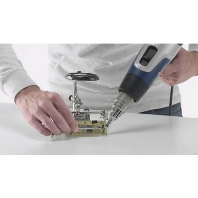 Eine Person lötet eine Leiterplatte mit einem Heißluftgerät. Sie hält die Platine auf einem Halter, während das Gerät in der anderen Hand ist.