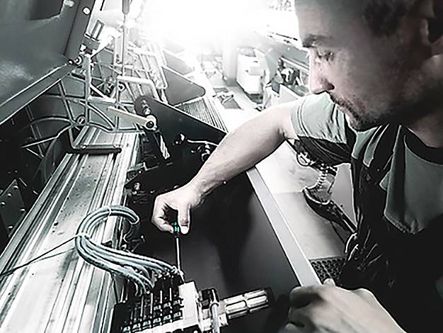 Eine Person, die mit Maschinen arbeitet, Komponenten mit einem Werkzeug justiert und sich auf mechanische Ausrüstung in einem industriellen Umfeld konzentriert.