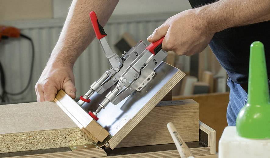 'Ein Handwerker montiert zwei Möbelteile mit einer Zwinge in einer Werkstatt.'