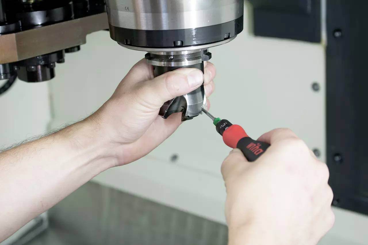 Eine Person hält ein Werkzeug in der Hand, während sie mit einem elektrischen Schraubendreher an einer Metallmaschine arbeitet.