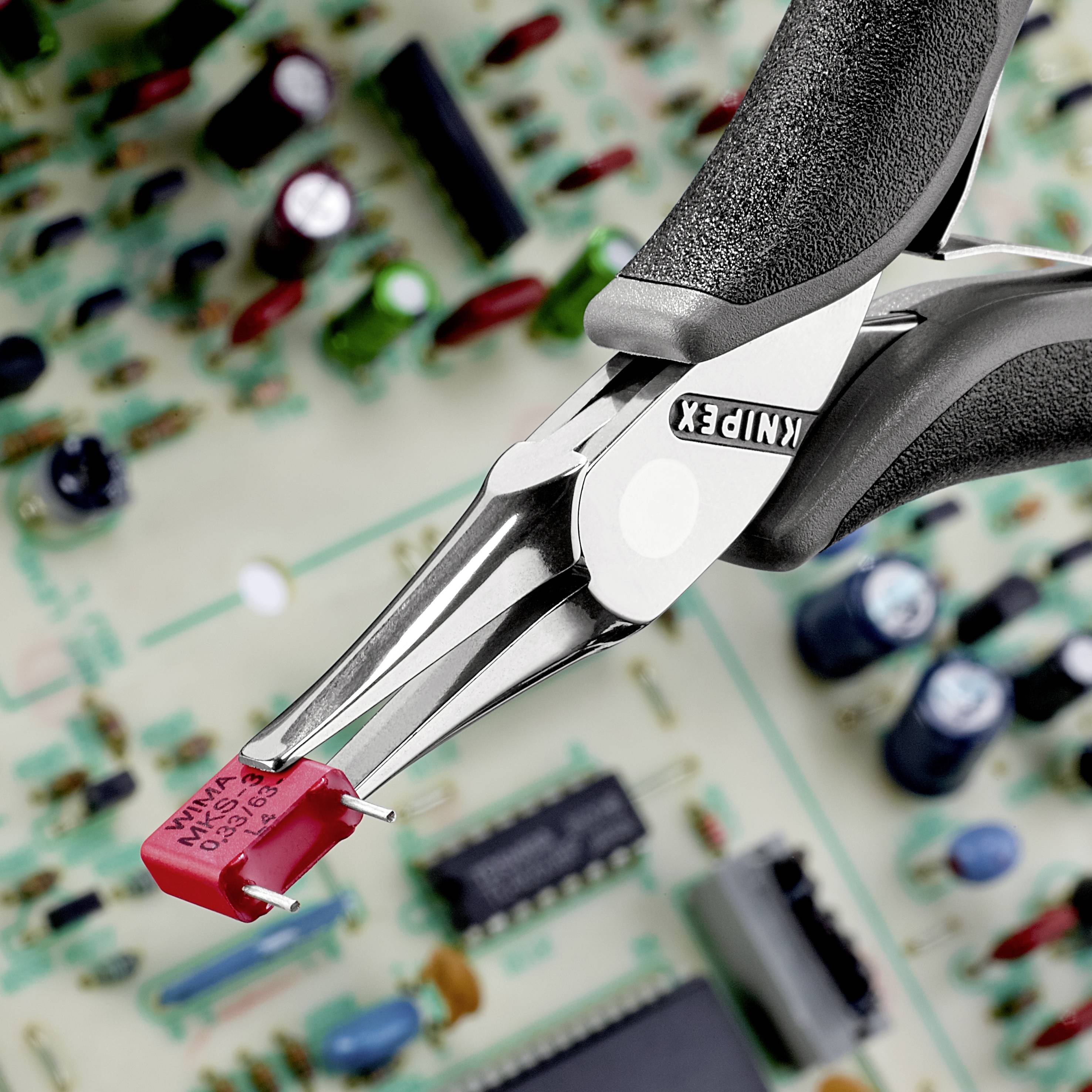 'Spitzzange hält roten elektronischen Widerstand auf einer Platine. Im Hintergrund unscharfe elektronische Bauteile.'