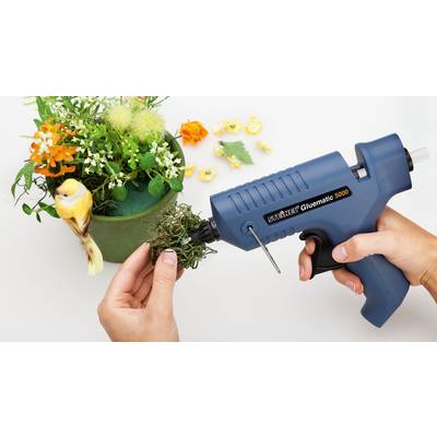 Eine Person dekoriert einen grünen Blumentopf mit künstlichem Moos und einer Kunststoffpistole für Heißkleber. Ein künstlicher Vogel sitzt am Rand.