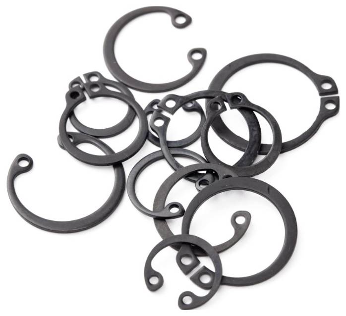 Eine Sammlung von verschiedenen schwarzen Sicherungsringen in unterschiedlichen Größen, die zufällig angeordnet sind und zum Sichern von Bolzen in Maschinenverbindungen verwendet werden.