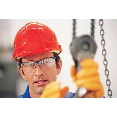 Ein Bauarbeiter mit rotem Schutzhelm und Schutzbrille steht vor unscharfem Hintergrund und bedient eine Kette mit einem Hebezeug.