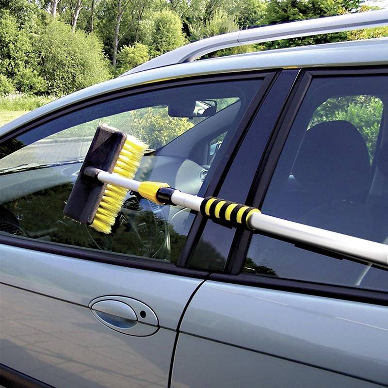 Ein Auto wird mit einer Waschbürste gereinigt. Die weiße Bürste hat gelbe Borsten und ist an einem langen Stiel befestigt.