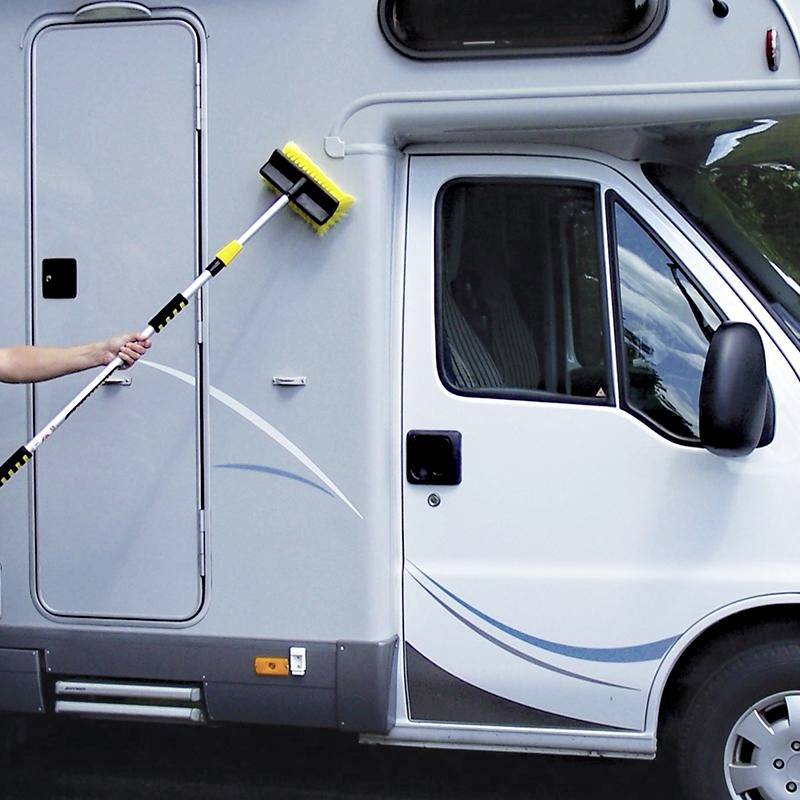 Person reinigt weiß-graues Wohnmobil mit langem Bürstenstiel. Fenster und Tür des Fahrzeugs sind sichtbar.
