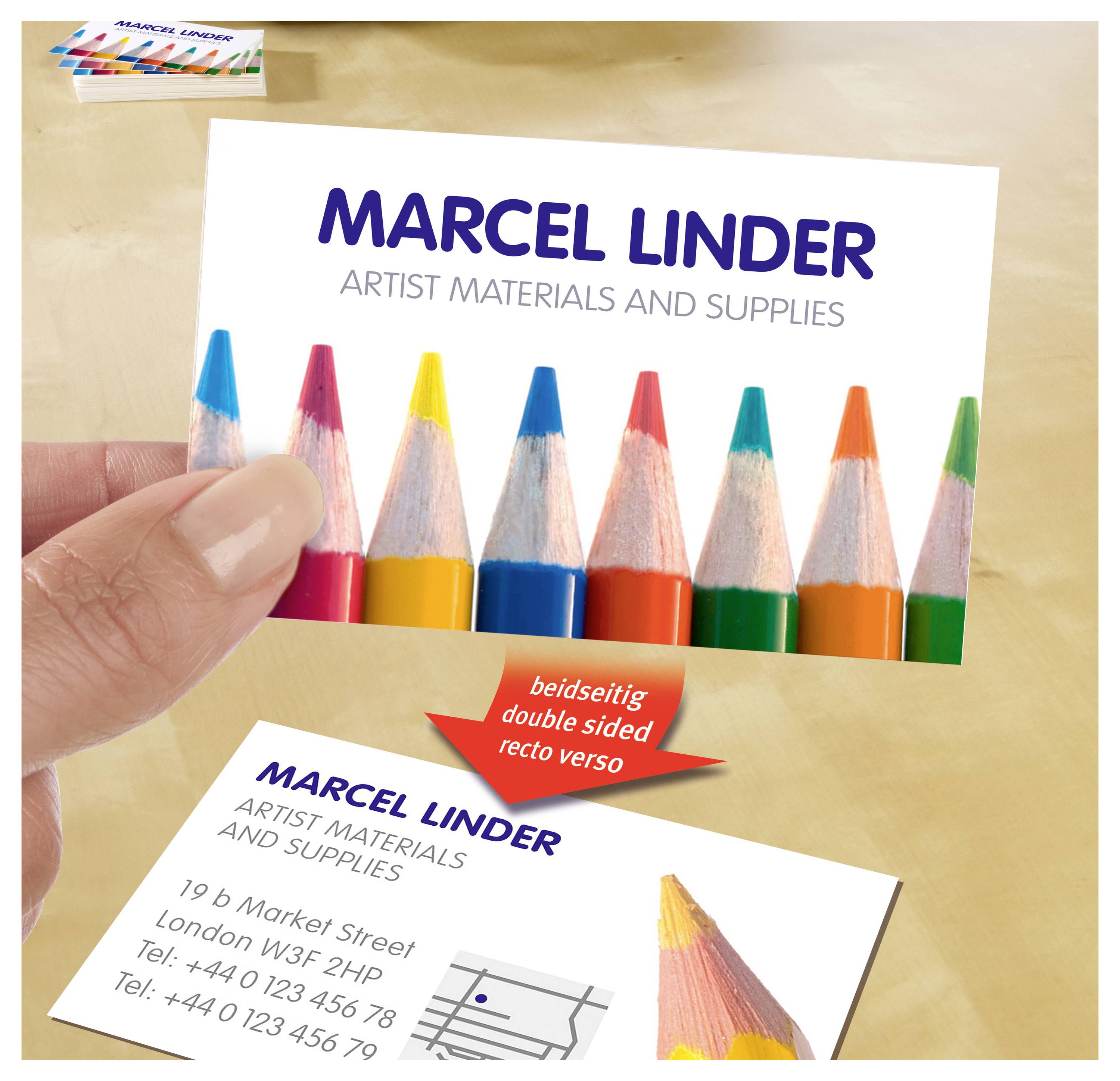 Hand hält Visitenkarte mit bunten Farbstiften und dem Text 'MARCEL LINDER – ARTIST MATERIALS AND SUPPLIES'; unten liegt eine weitere Karte mit Kontaktdaten und Karten-Symbol, Pfeil weist auf beidseitigen Druck hin.