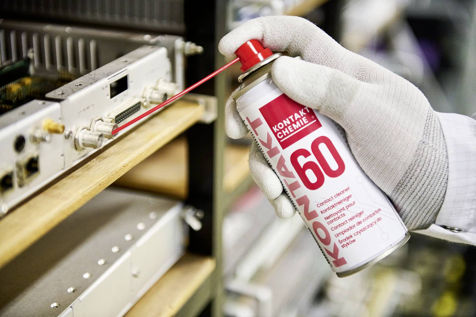 Eine Person mit Handschuhen wendet ein Elektronik-Sprühmittel in einer Werkstatt an, um elektronische Geräte zu reinigen und schützen.