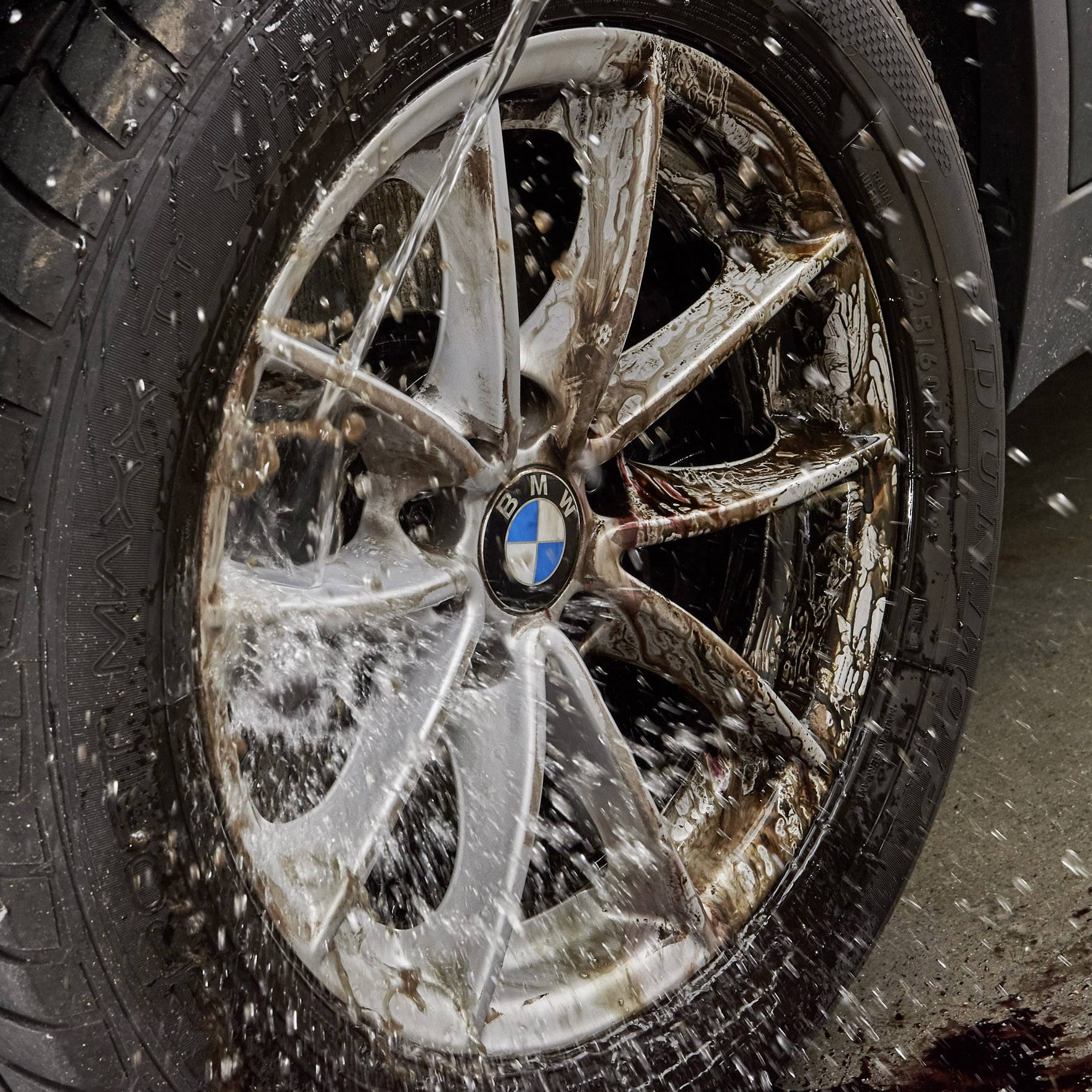 Ein Autoreifen wird mit Wasser bespritzt. Die Felge gehört zu einem BMW. Das Bild zeigt die dynamische Bewegung des Wassers.