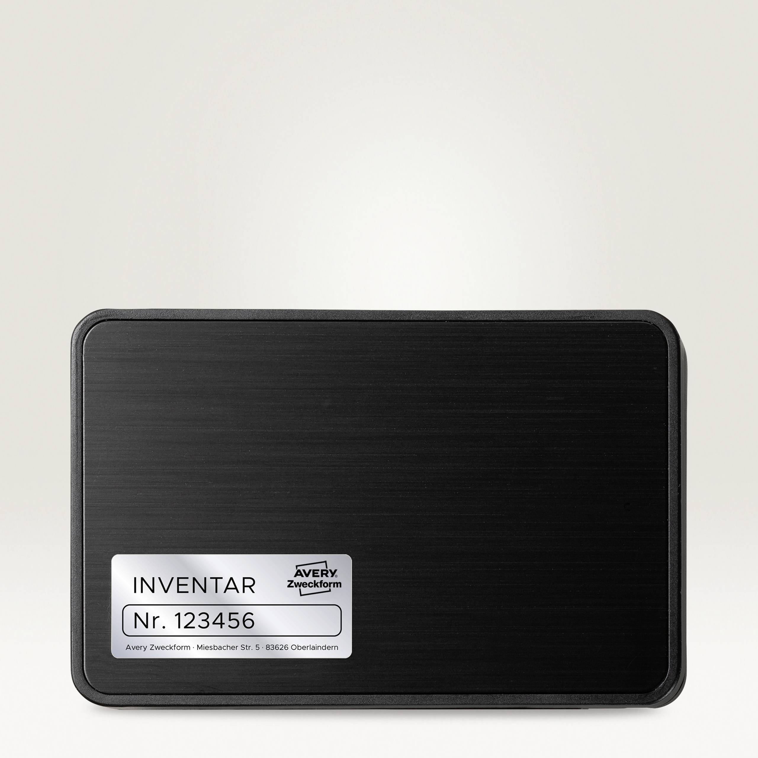 Ein rechteckiges, schwarzes Inventaretikett mit der Aufschrift 'Inventar Nr. 123456' erscheint auf einem hellen Hintergrund.