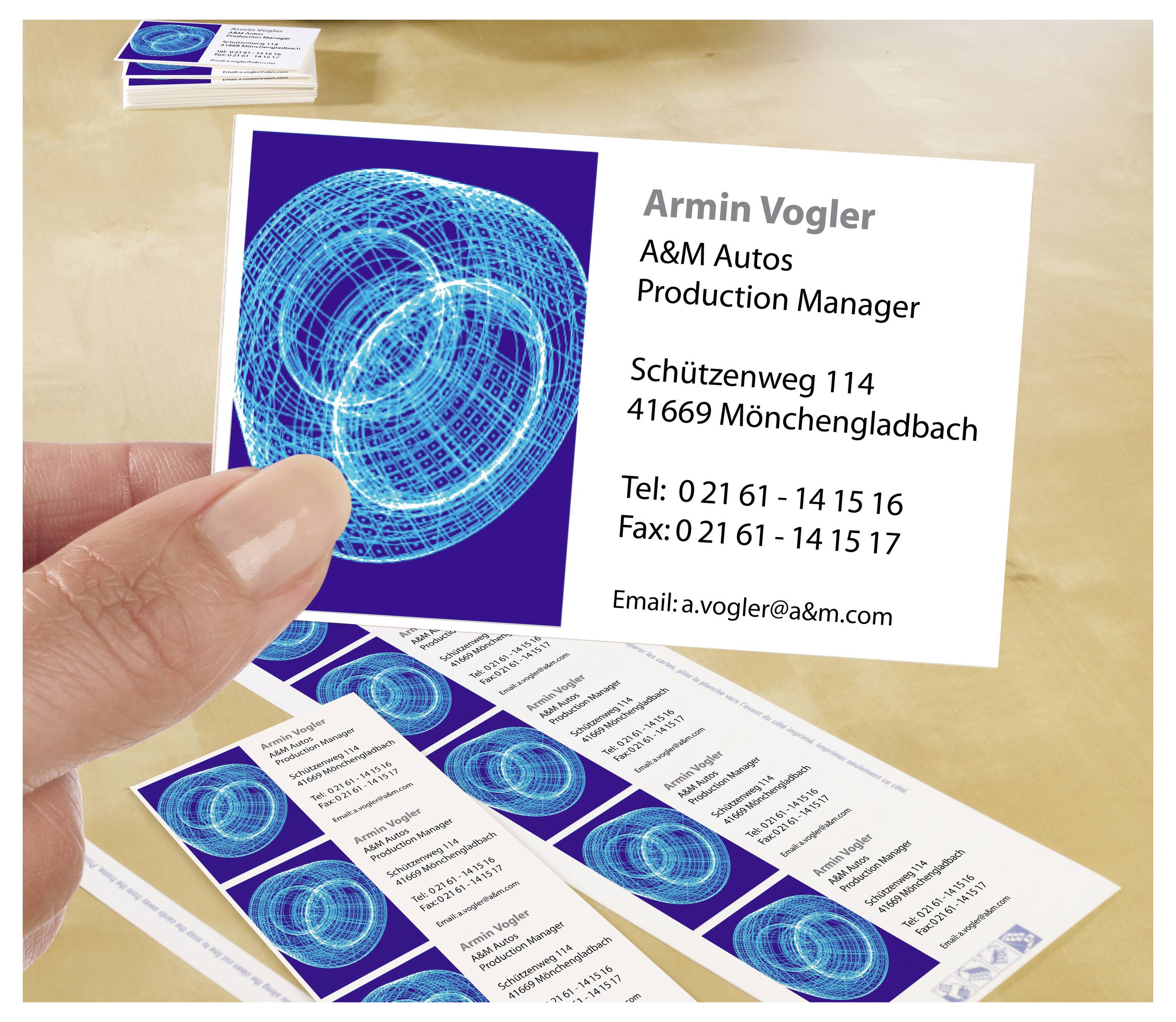 Hand hält eine Visitenkarte von Armin Vogler, A&M Autos, Production Manager, mit Adresse, Telefon, Fax und E-Mail; weitere Karten liegen daneben.<br>