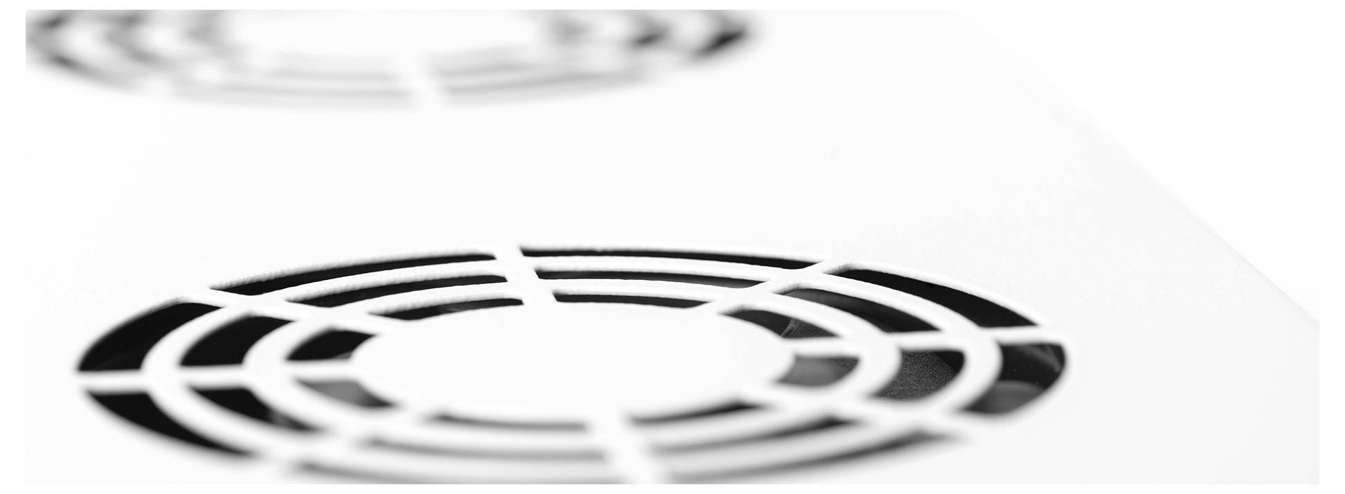 Nahaufnahme einer weißen Oberfläche mit zwei kreisförmigen Metallgittern, die in einem Muster angeordnet sind und leicht verschwommene Schatten auf der Oberfläche werfen.