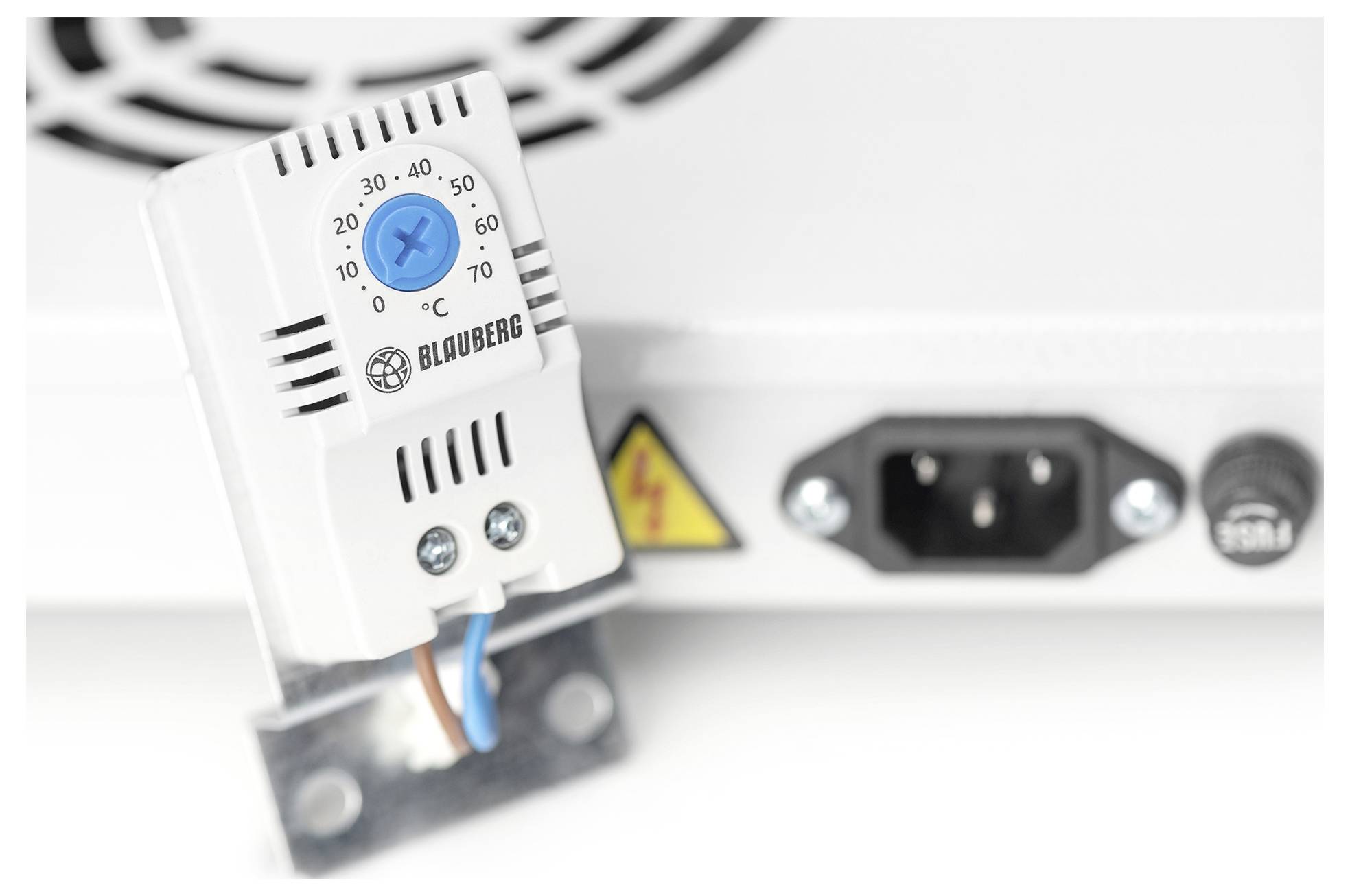 Ein weißes Thermostat mit einem blauen Einstellregler, der Temperaturen von 0 bis 60°C anzeigt, montiert in der Nähe eines Elektrogeräts mit einer Steckdose.