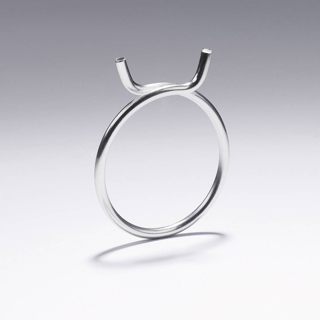 Ein silberner Ring in minimalistischer Form, mit einer offenen, geschwungenen Spitze, die nach oben zeigt, auf grauem Hintergrund.