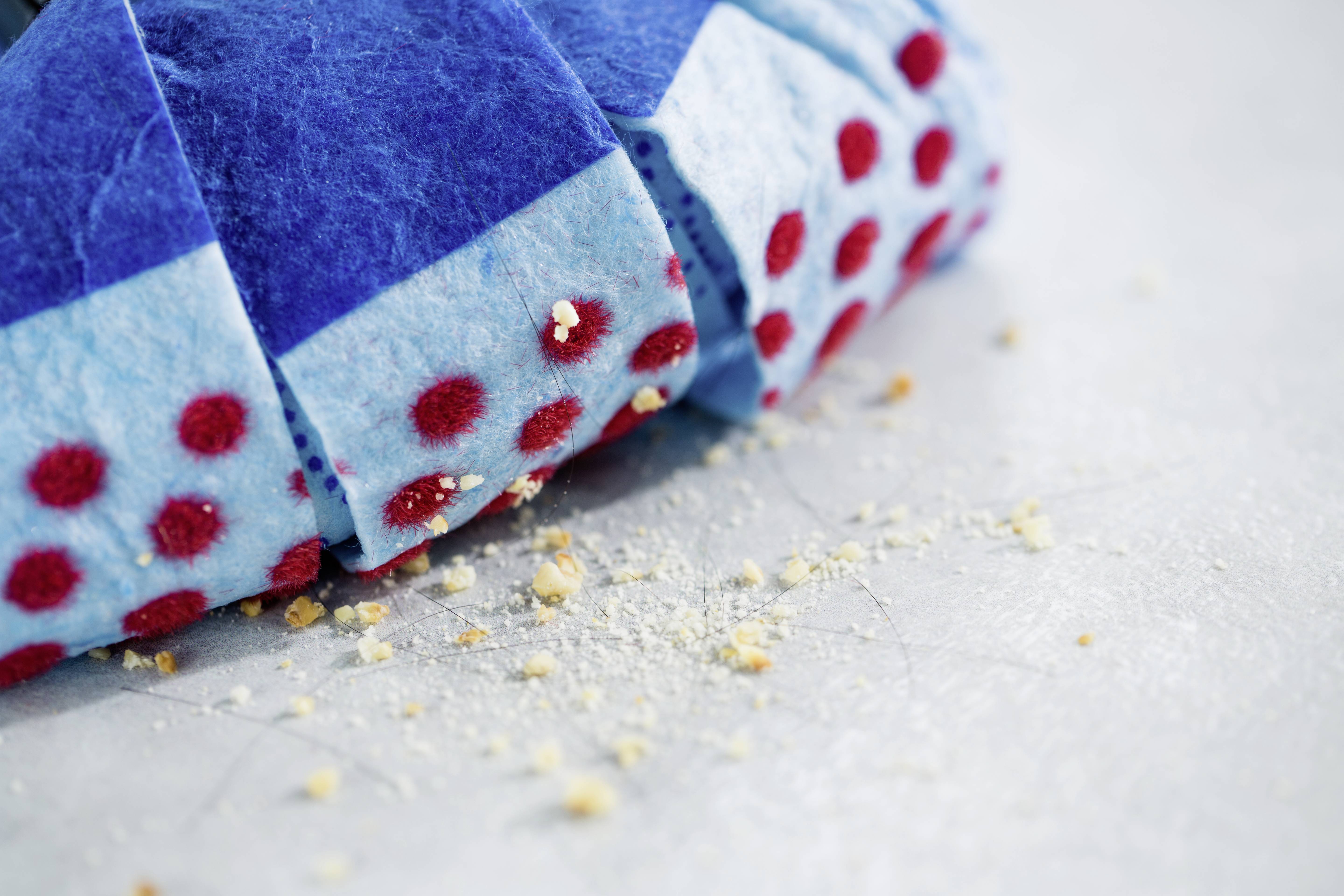 Ein blauer Kehrbesen mit roten Punkten entfernt Krümel von einer weißen Oberfläche.