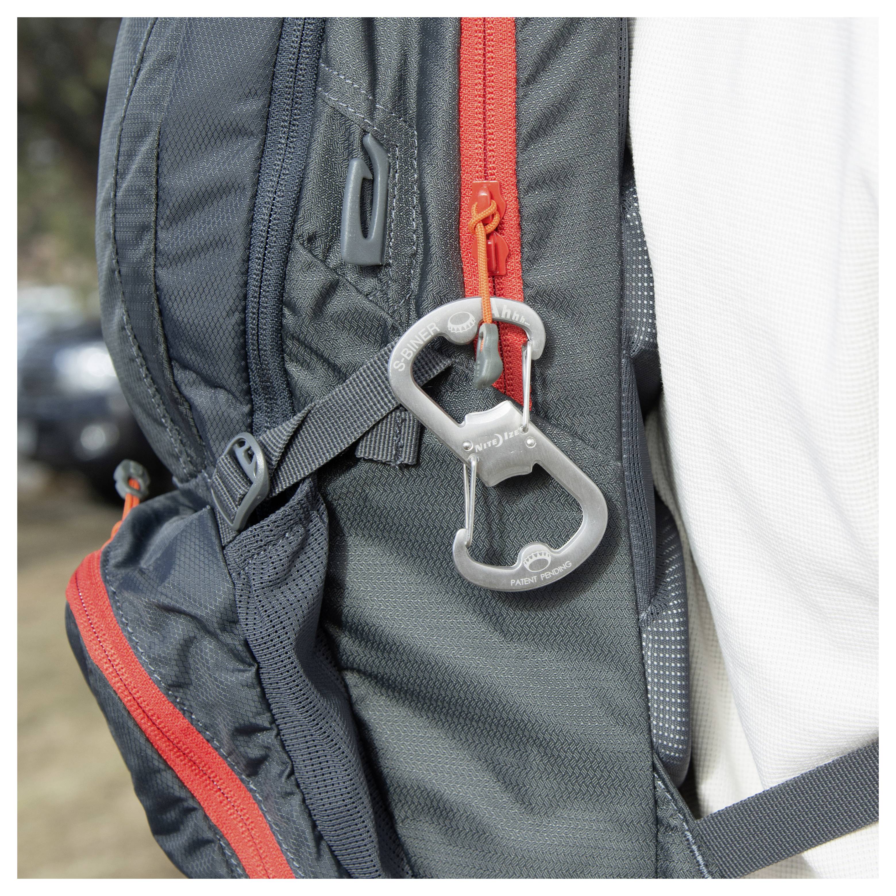 Ein Rucksack mit roten Reißverschlüssen und einem Karabiner, der an einer Schlaufe an der Seite befestigt ist. Der Rucksack wird von einer Person in einem weißen T-Shirt getragen.