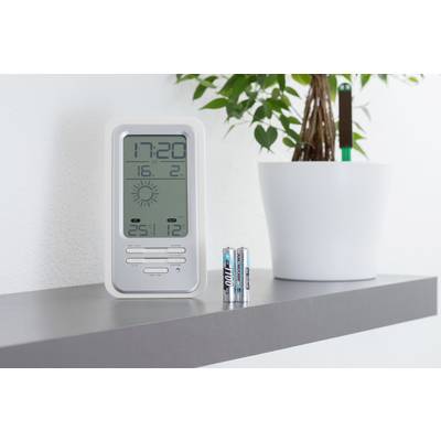 Ein digitales Thermo-Hygrometer zeigt die Uhrzeit 17:20, Temperatur 25,1°C, Luftfeuchtigkeit 12%, steht auf einem Regal neben einem Blumentopf.