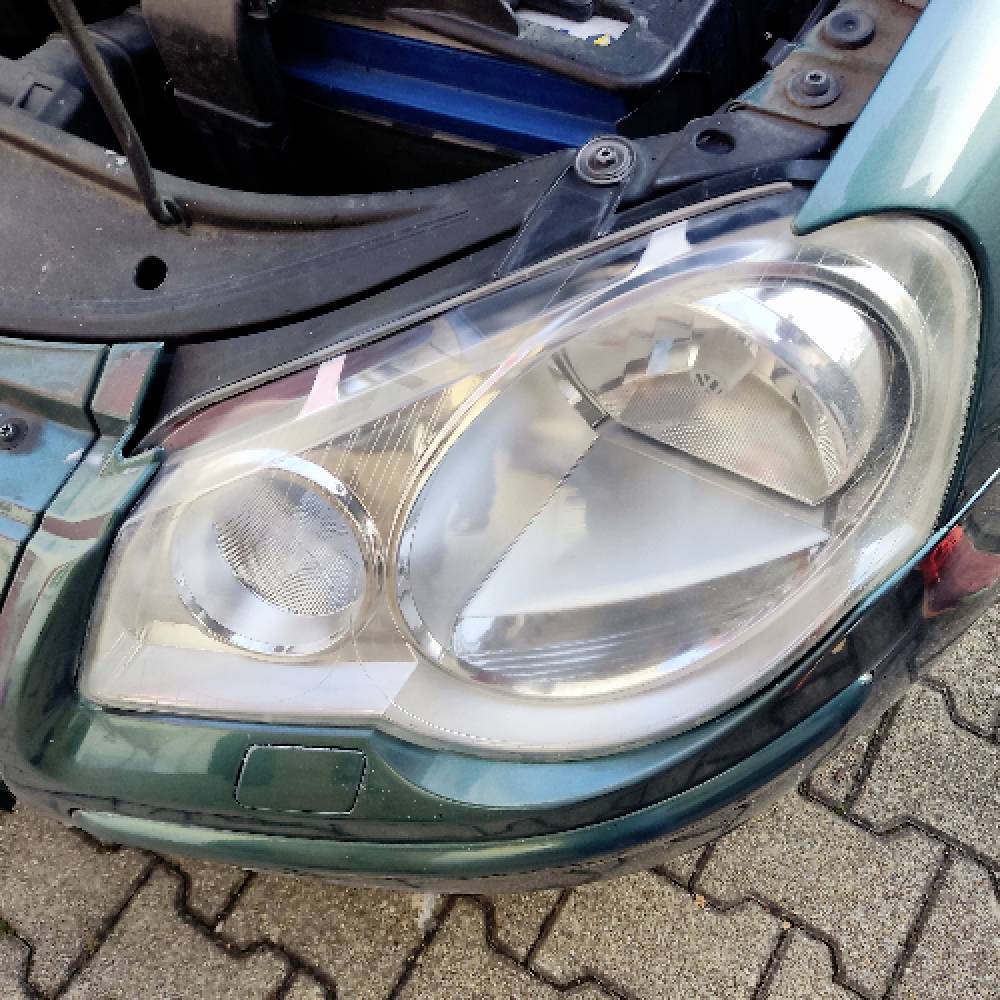 Nahaufnahme des linken Scheinwerfers und eines Teils des Stoßfängers eines grünen Autos, die Details des Scheinwerferdesigns und dessen Positionierung zeigen.