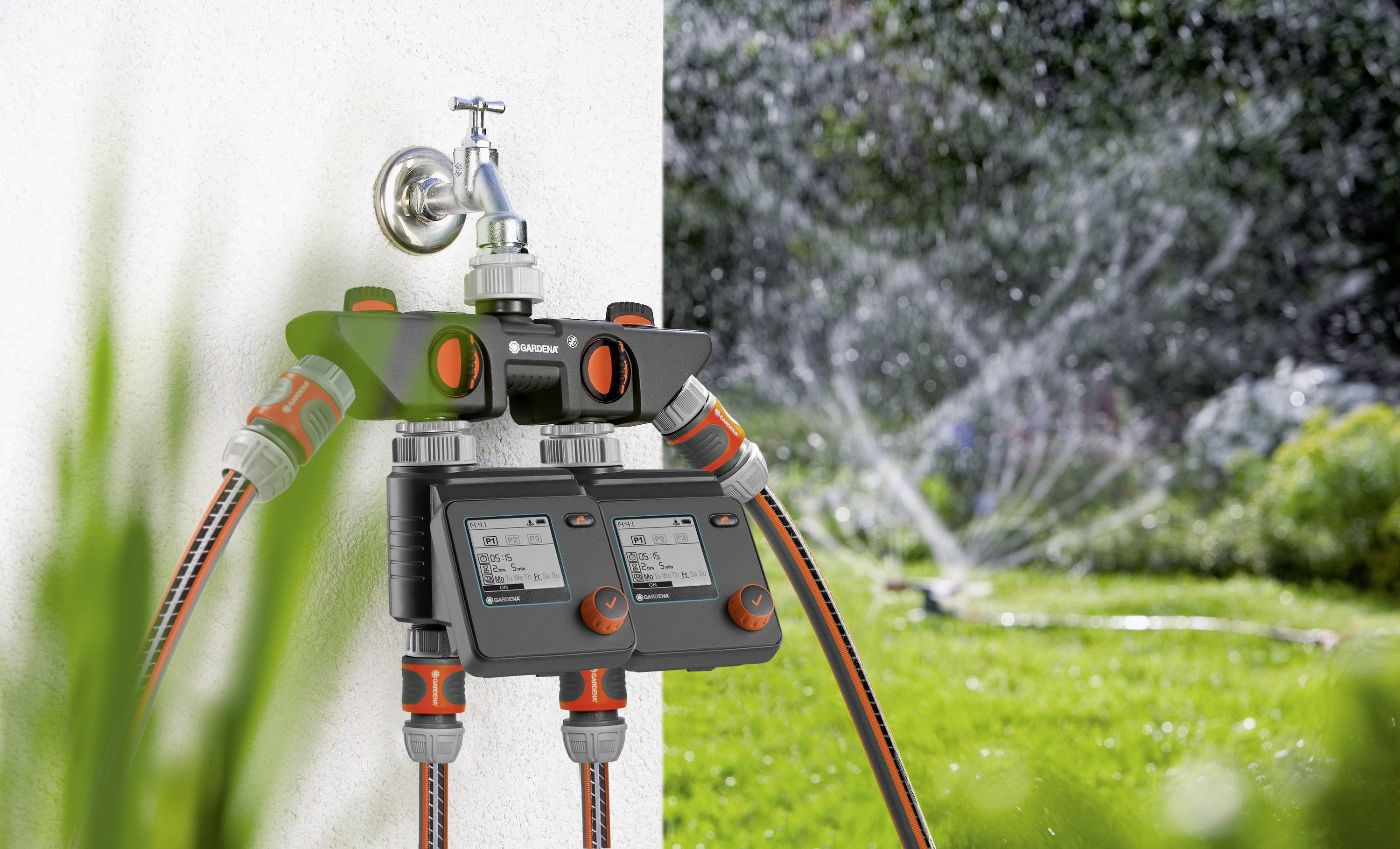 Ein automatisches Bewässerungssystem ist an einen Wasserhahn angeschlossen. Im Hintergrund läuft ein Rasensprenger auf einer grünen Fläche.